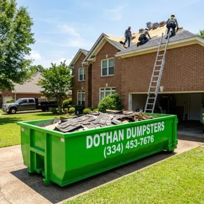 Roofing dumpster rental in Dothan AL with green Dothan Dumpsters container full of shingle debris during a roof replacement
